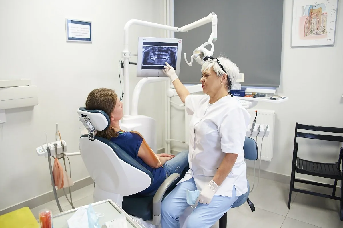 Lekarka omawia z pacjentką zdjęcie pantomograficzne wyświetlone na monitorze w gabinecie